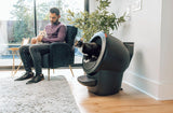 cat using Litter-Robot 4 with LitterHopper while man sits with another cat on his lap
